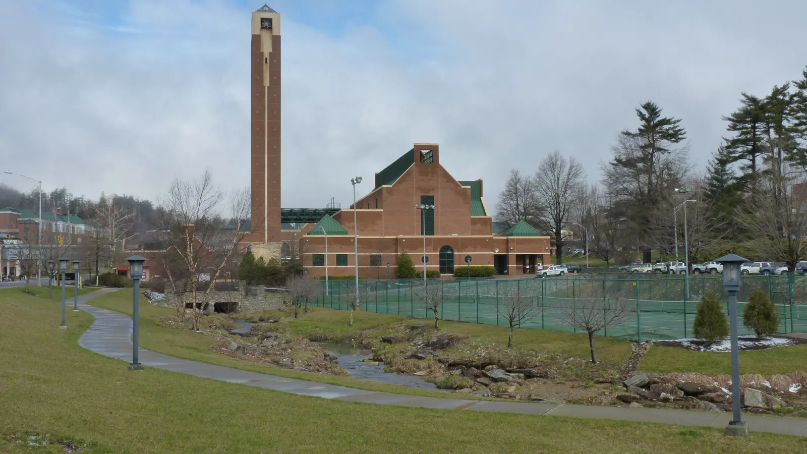 A tall brick tower and brick building beside a creek, a walkway and tennis courts on the Appalachian State University campus in Boone