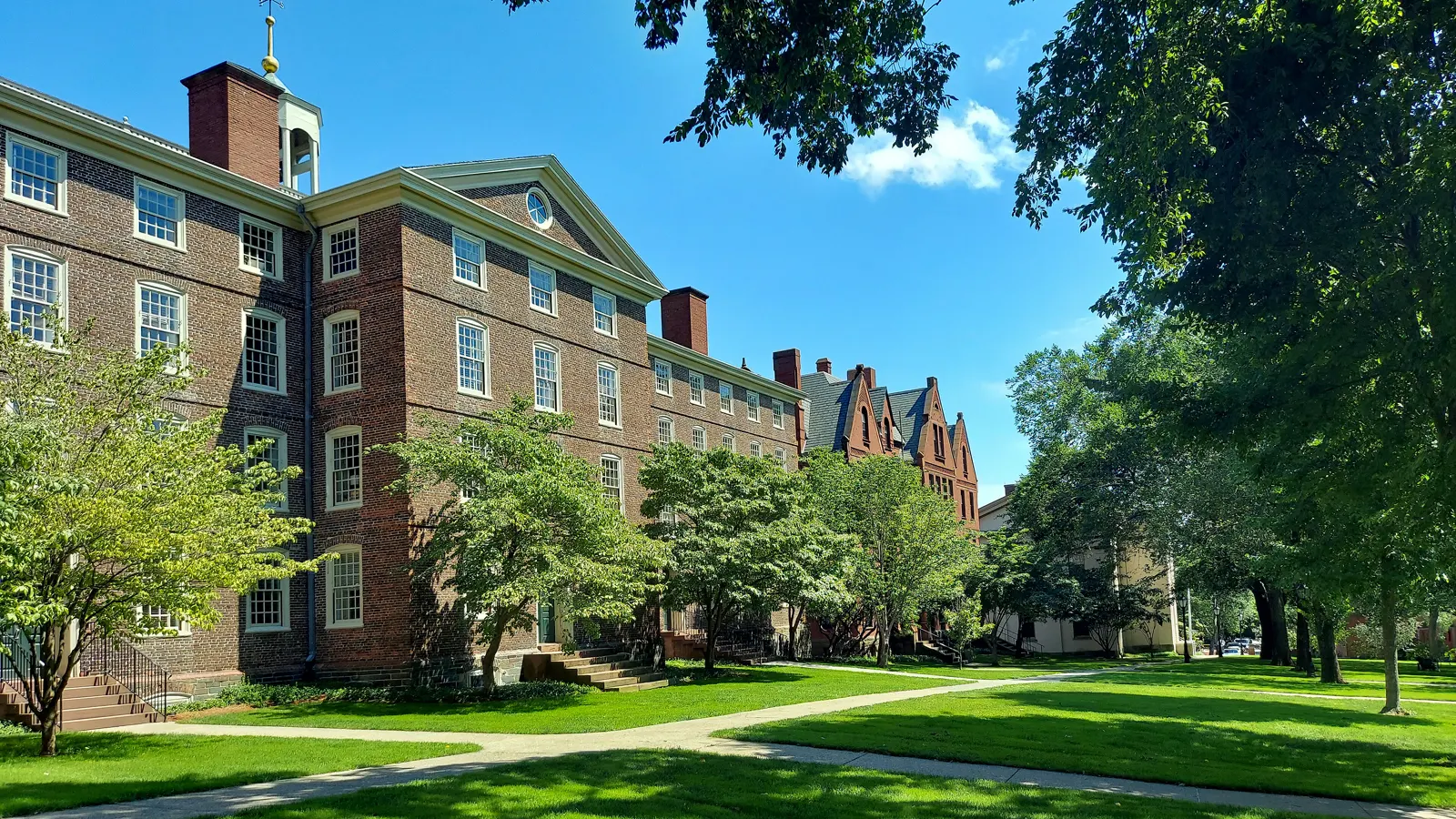 Red brick colonial-era hall with a cupola, trees and lawns on the Brown University campus