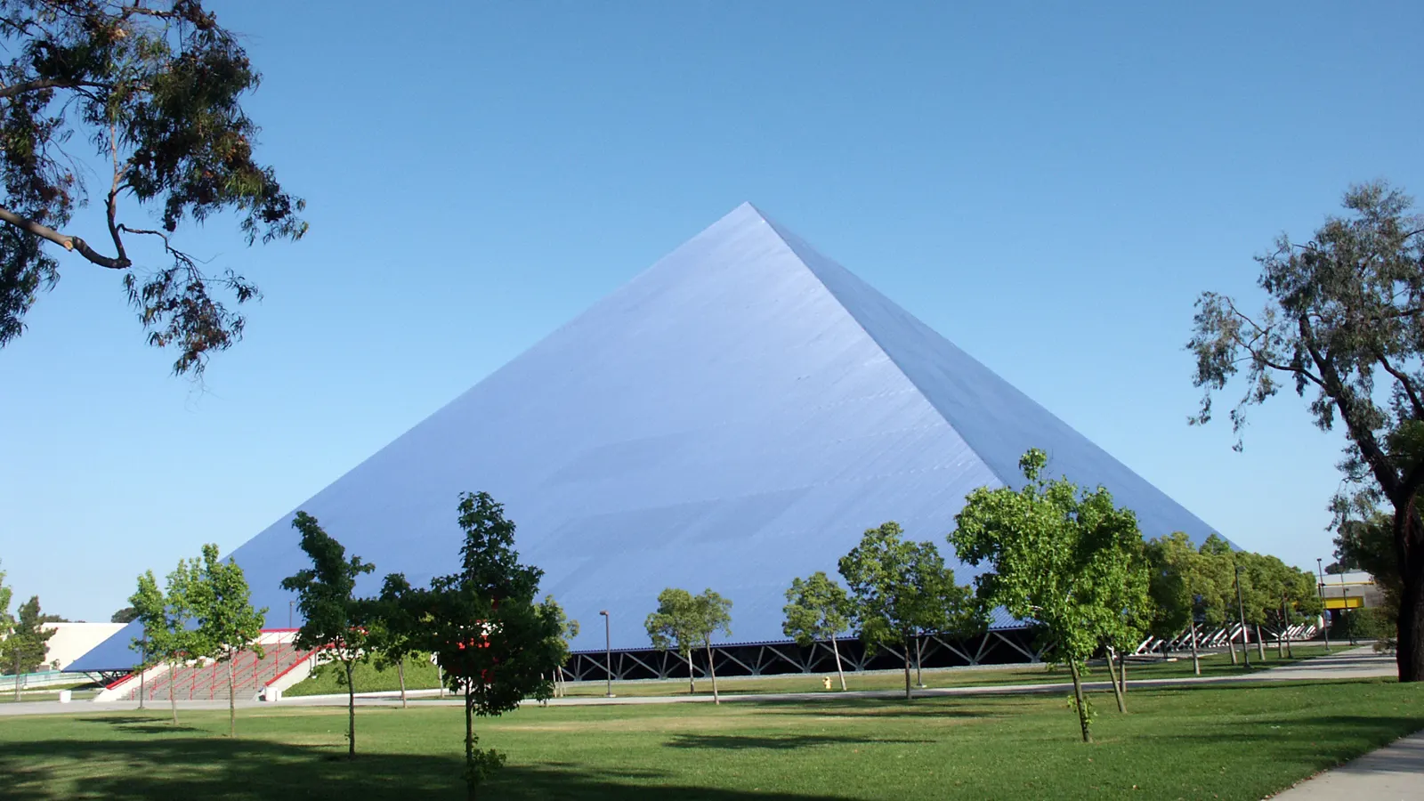 The Walter Pyramid arena at Cal State Long Beach under a clear sky, with lawn and young trees in front