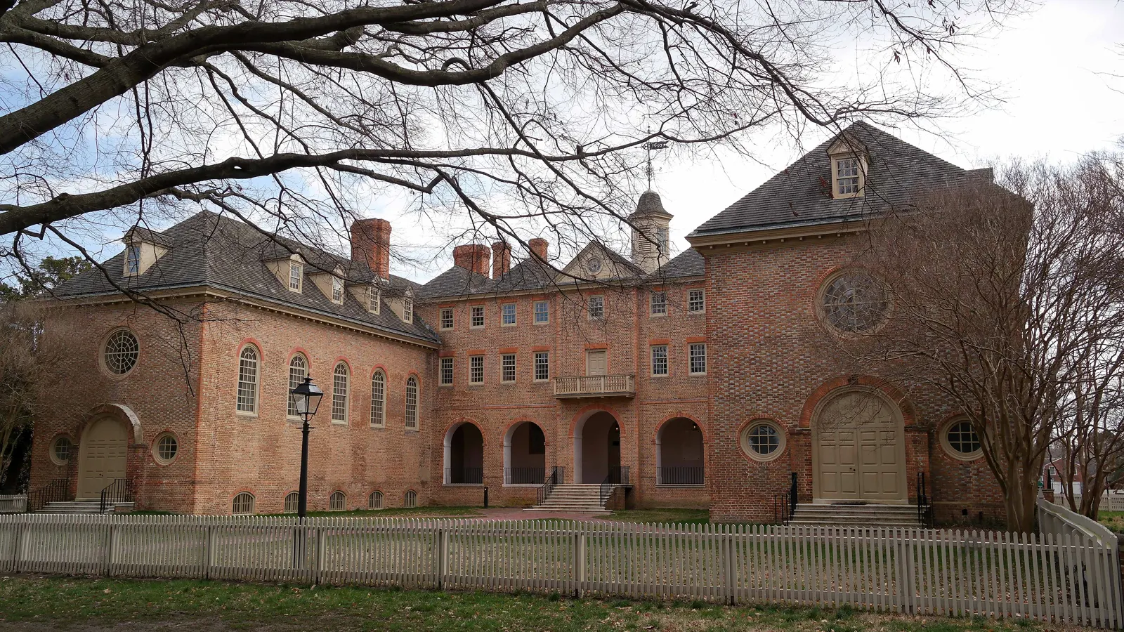 The brick Wren Building behind a white picket fence at William and Mary in Williamsburg, Virginia