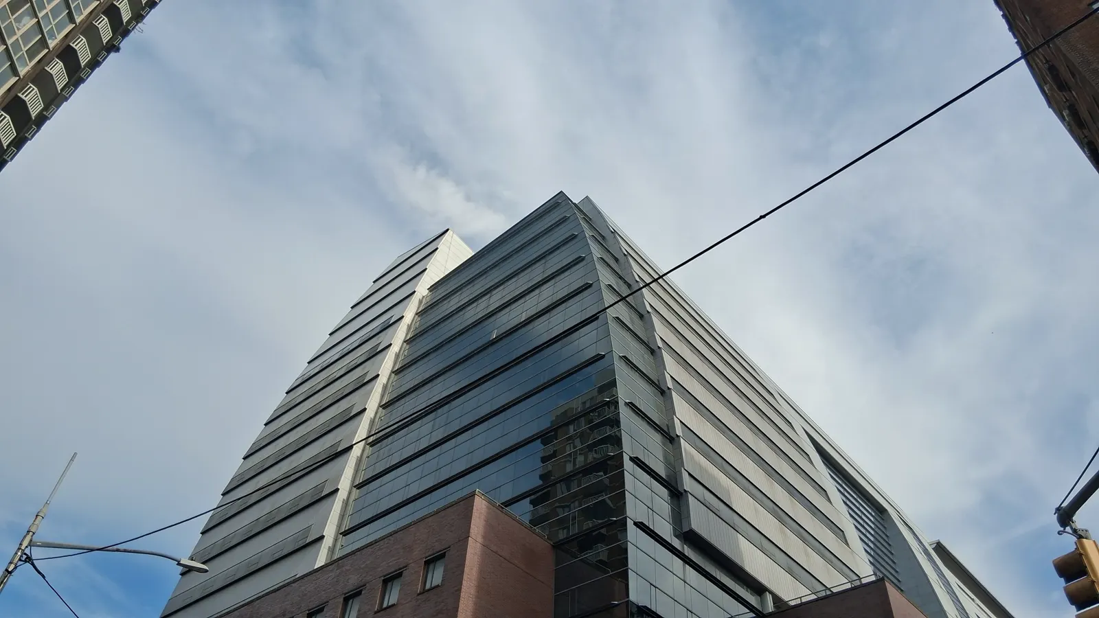 Looking up at Baruch College's glass Newman Vertical Campus tower against a cloudy sky