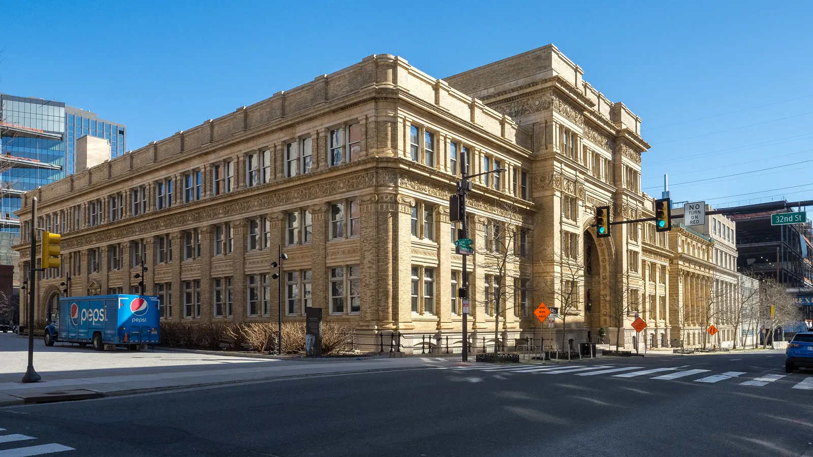 Drexel University's Main Building, a tan stone building on a street corner at 32nd Street in Philadelphia, under a clear blue sky