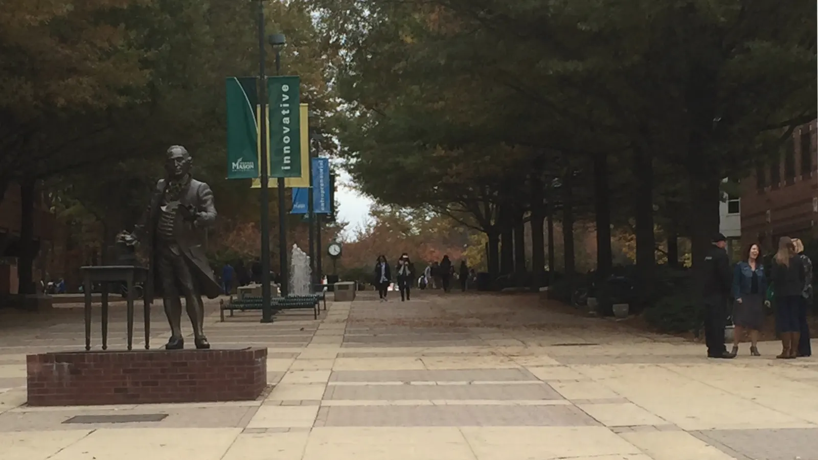 The bronze George Mason statue beside a tree-lined walkway on the Fairfax campus in autumn
