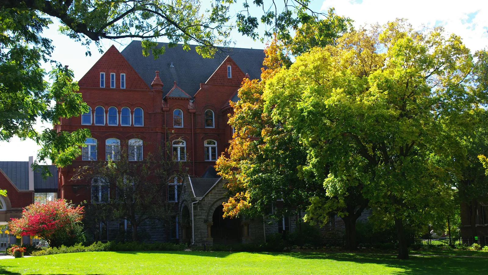 Old Main, the red brick hall behind a green lawn and autumn trees at Macalester College in Saint Paul, Minnesota
