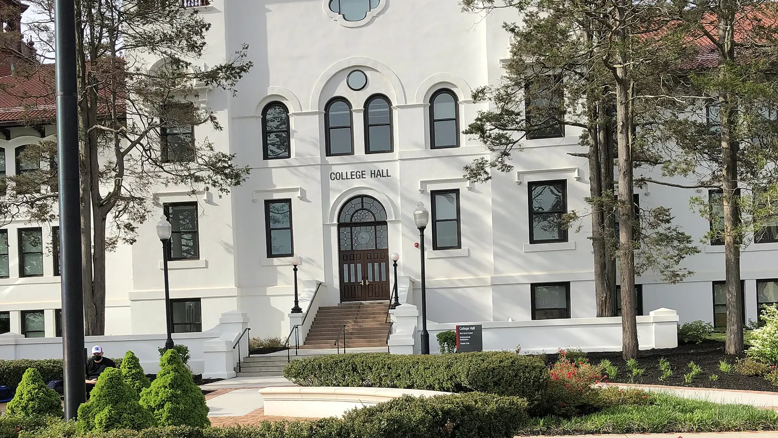 The white facade of College Hall behind trees and flower beds at Montclair State University in Montclair, New Jersey