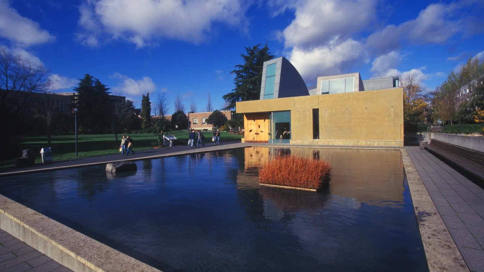 The Chapel of St. Ignatius at Seattle University, a tan building with light towers, behind its reflecting pool under a blue sky with clouds