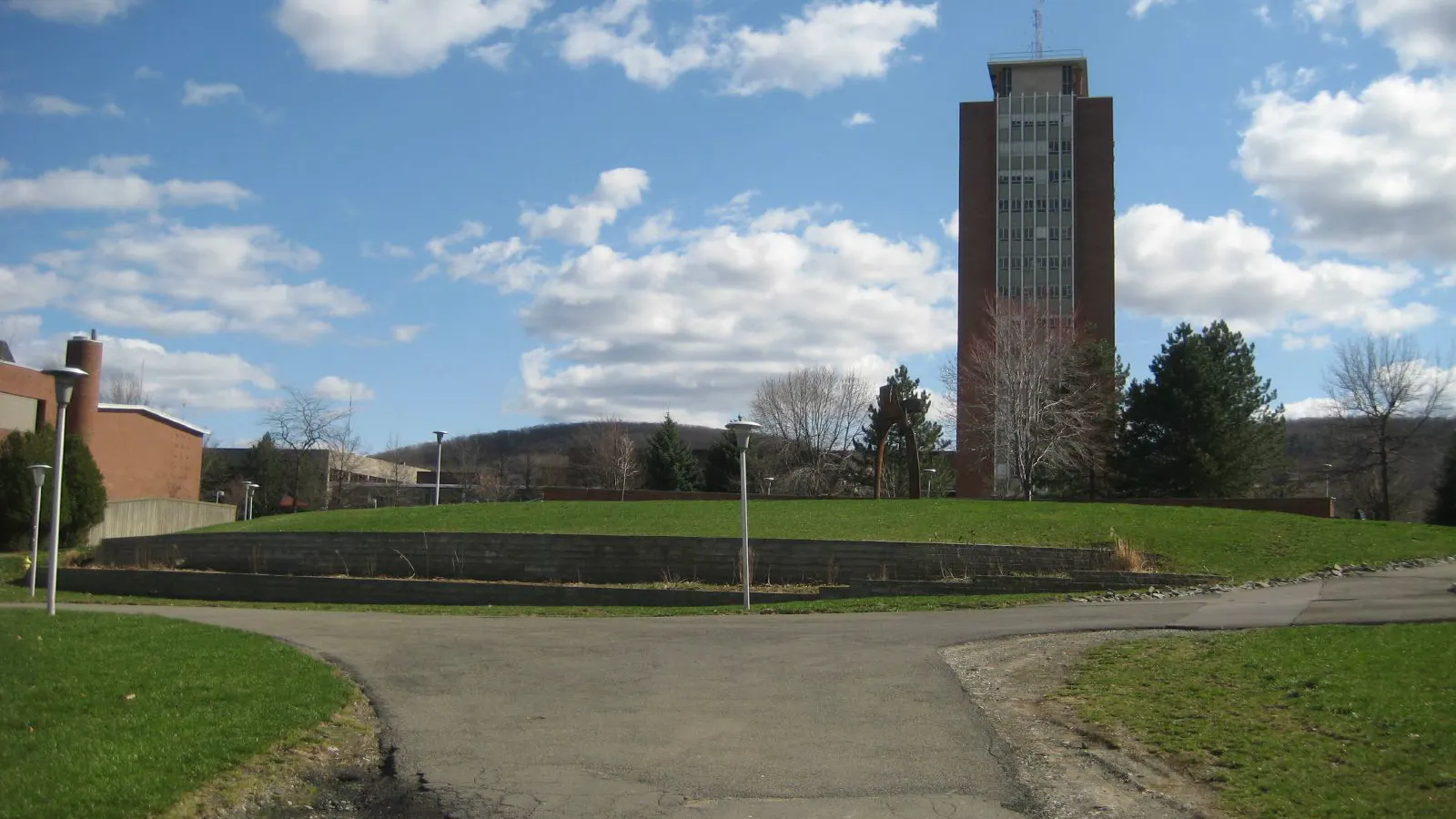 The library tower rising behind a green lawn on the Binghamton University campus under a blue sky
