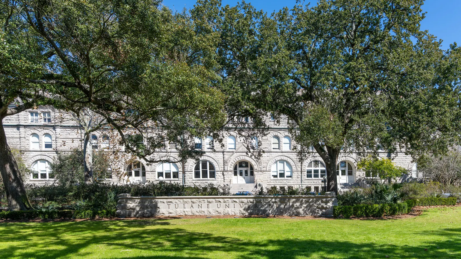 Gibson Hall, a Romanesque stone building behind live oaks and a lawn at Tulane University