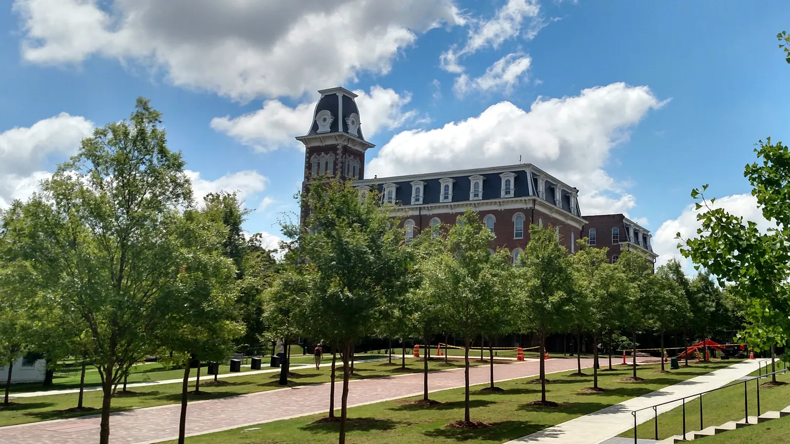 Old Main and its clock tower behind a tree-lined walk on the University of Arkansas campus in Fayetteville