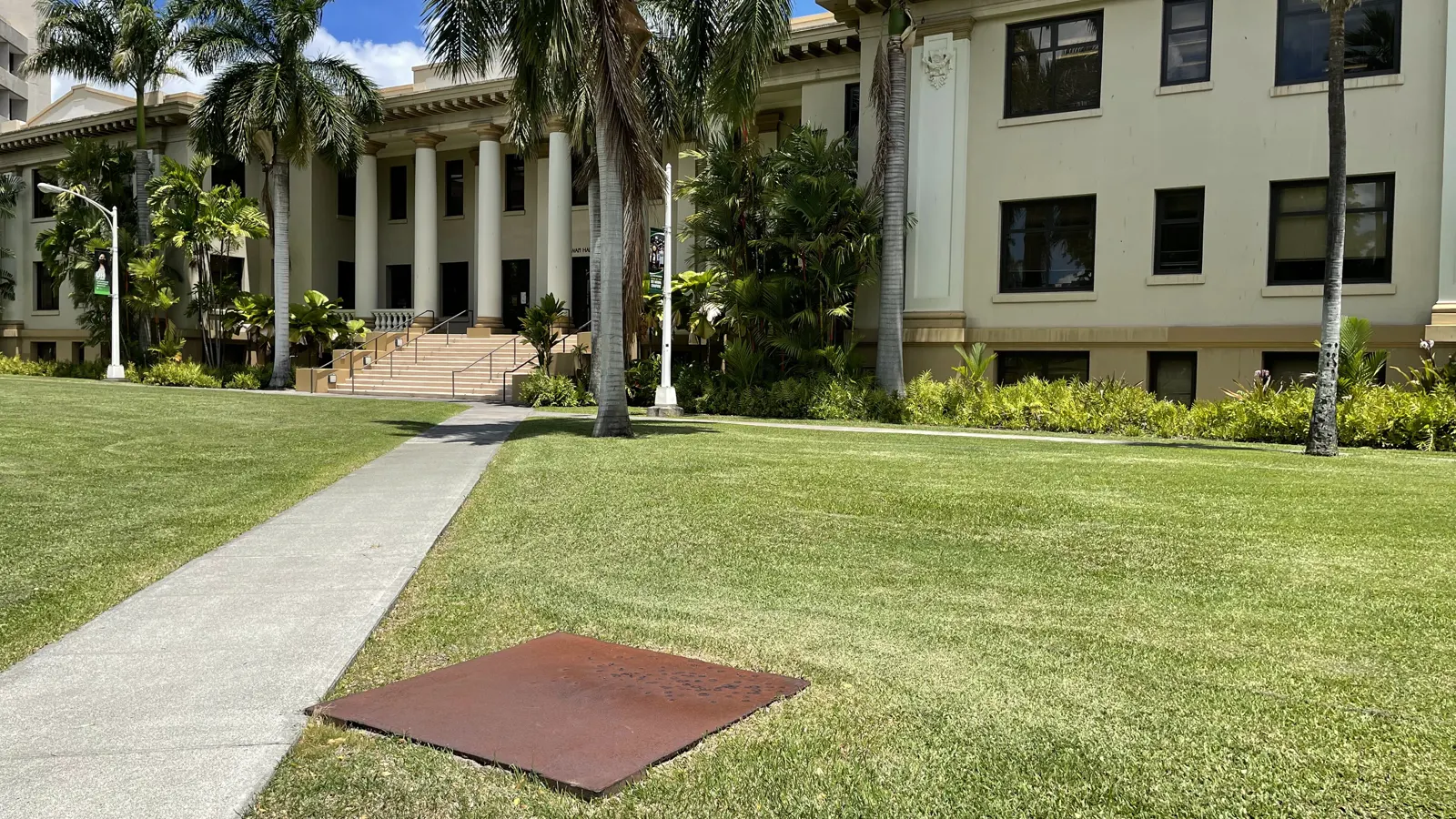 Hawaii Hall with its columned entrance behind palms and a lawn on the University of Hawaii at Manoa campus in Honolulu