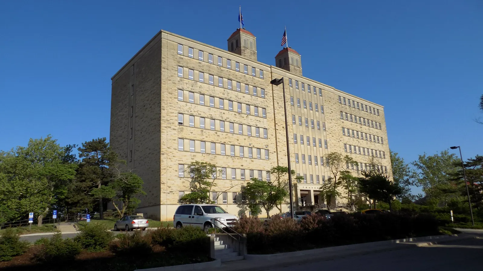 Fraser Hall, a tall limestone building with two red-capped towers and flags, under a clear blue sky at the University of Kansas