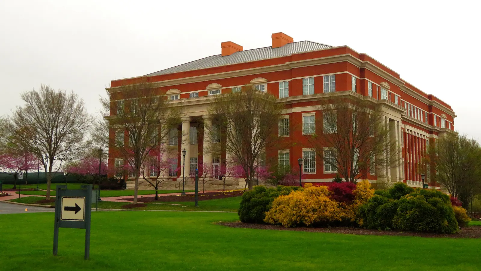 A red brick building with white columns behind a lawn and flowering shrubs on the UNC Charlotte campus