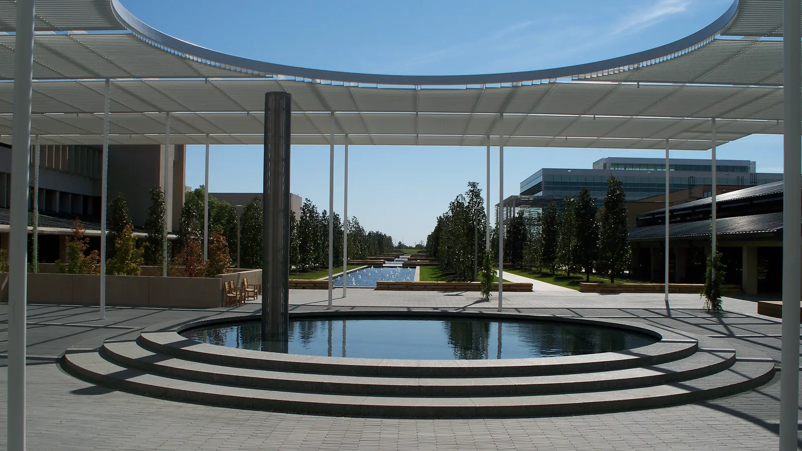 A round reflecting pool under a white shade canopy, looking down the tree lined main mall at the University of Texas at Dallas in Richardson, Texas